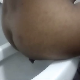 A dark-skinned woman takes a shit while sitting on a toilet. Visible poop action is seen from behind her ass. Subtle crackling and a single, loud, heavy plop is clearly heard. Over a minute.